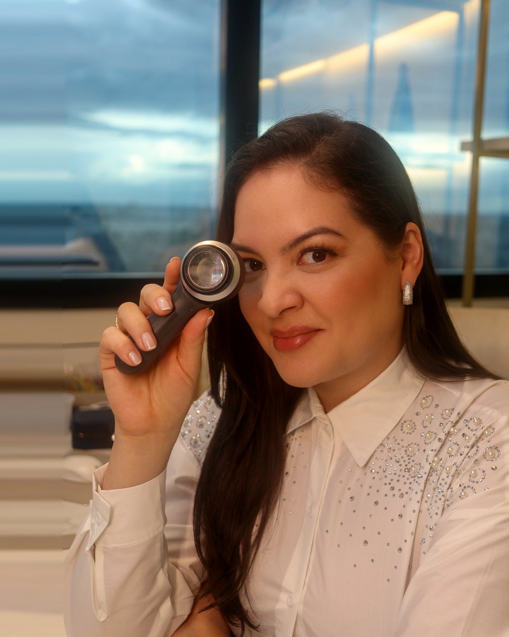 Dra. Aline Záu no consultório, com o dermatoscópio na mão.