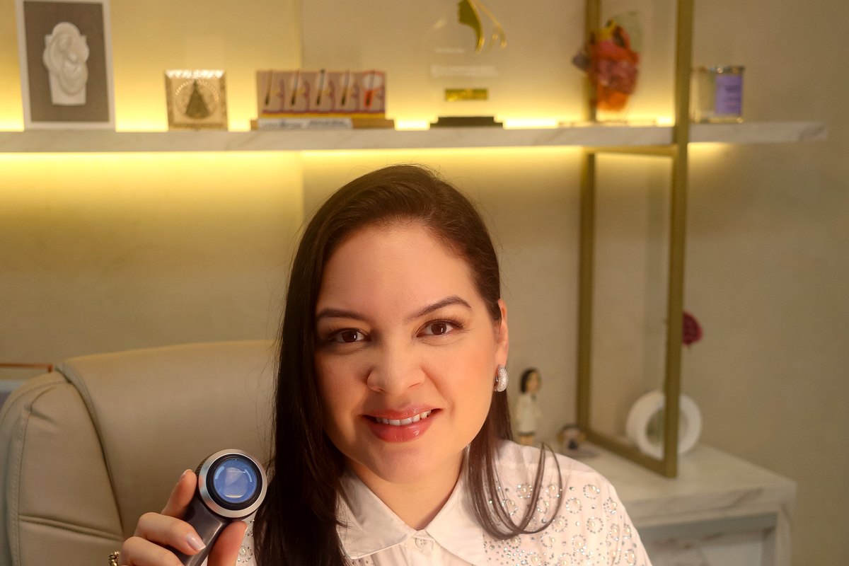 Dra. Aline Záu com o dermatoscópio aceso, no consultório.